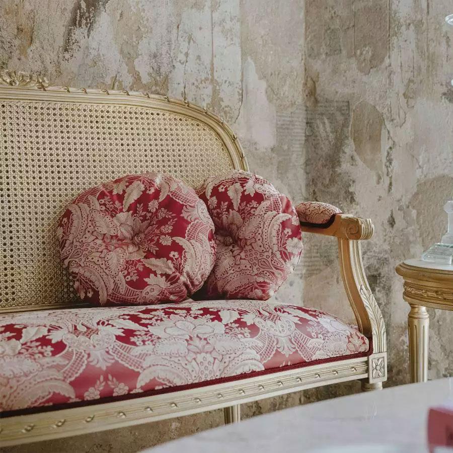Elegant traditional settee with cane back and red toile upholstery in distressed interior.