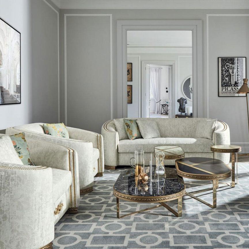Elegant traditional sofas in cream upholstery with gold accents arranged in a luxurious living room with gray walls and patterned rug.